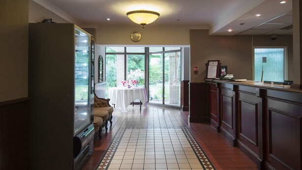 A hotel lobby with a reception desk, a clock, and a view of the garden through large glass doors. - Paddington House Hotel (Warrington)