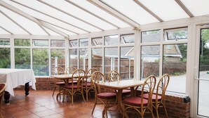 A conservatory with a tiled floor, wooden table, and wicker chairs. - Paddington House Hotel (Warrington)