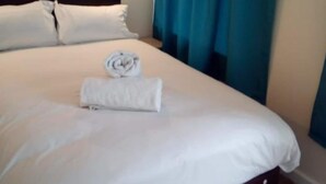 A neatly made bed with white linens and a rolled towel, a dark headboard, and a wall-mounted light fixture. - Paddington House Hotel (Warrington)