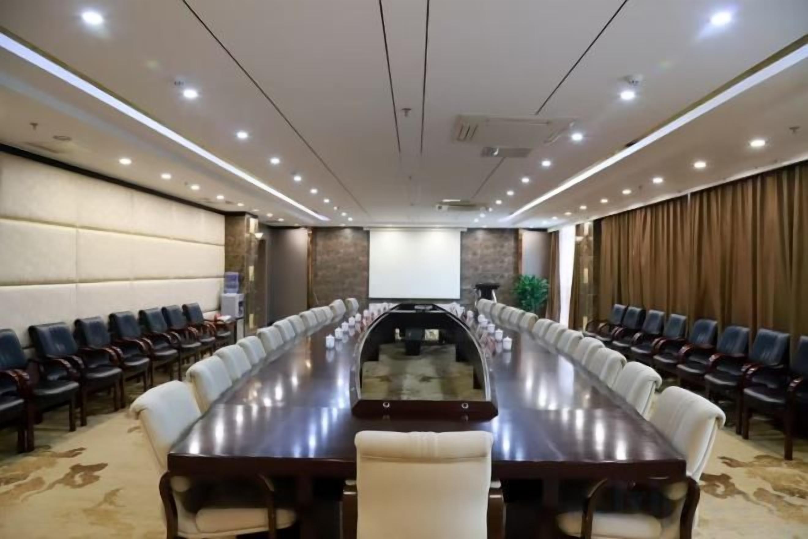 A conference room with a long table, chairs, a projector screen, and a carpeted floor.