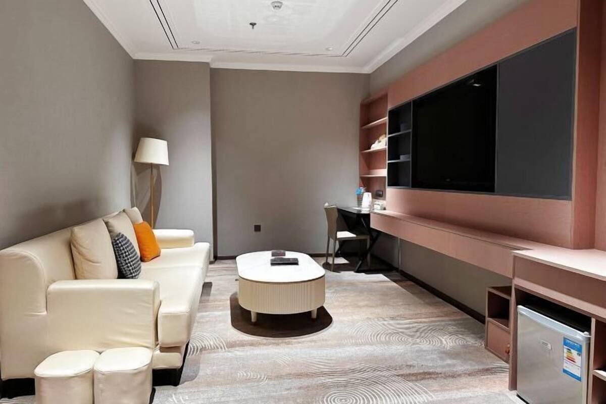 A modern living room with a sofa, ottoman, coffee table, and a flat-screen TV mounted on the wall.