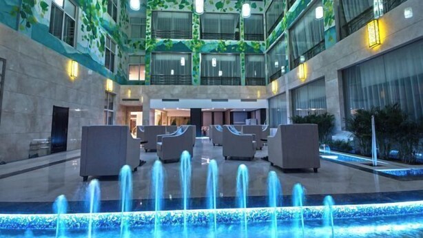 A hotel lobby with a fountain, seating areas, and a modern design with green leaf patterns on the walls. - Dongsheng · Yuyuan Hotel (Qixia)