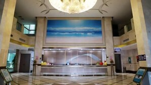 A spacious lobby with a large reception desk, a high ceiling with a chandelier, and a large painting of a blue sky. - Dongsheng · Yuyuan Hotel (Qixia)