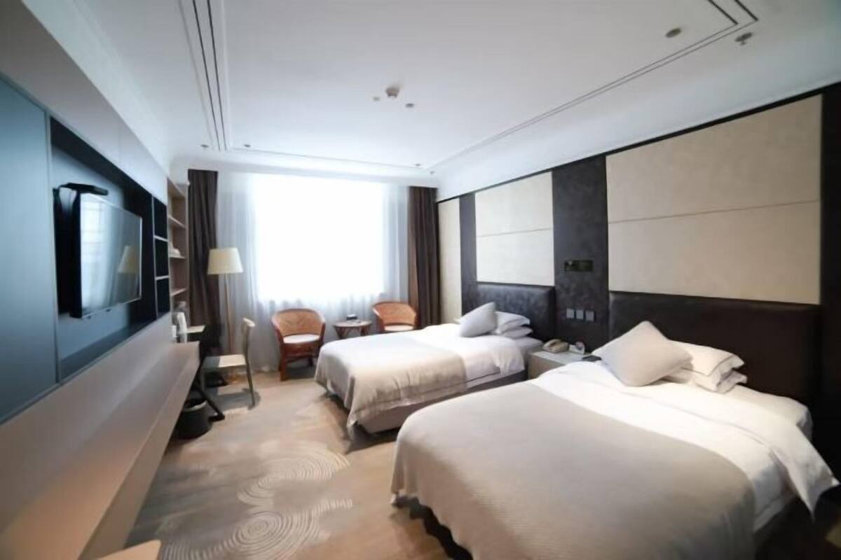 A hotel room with two beds, a TV, a desk, and a chair.