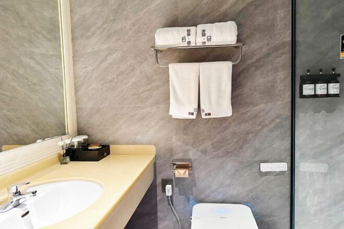 Un baño con pared de mármol, un lavamanos, un espejo, un perchero con toallas y un box de ducha de vidrio.