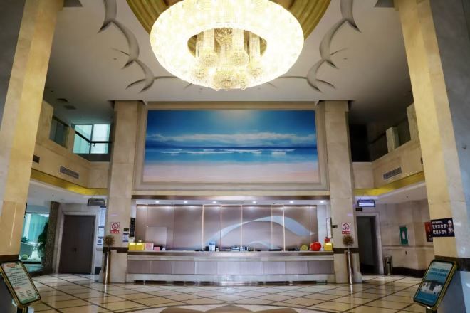 A hotel lobby with a reception desk, a large painting of a beach, and a chandelier.