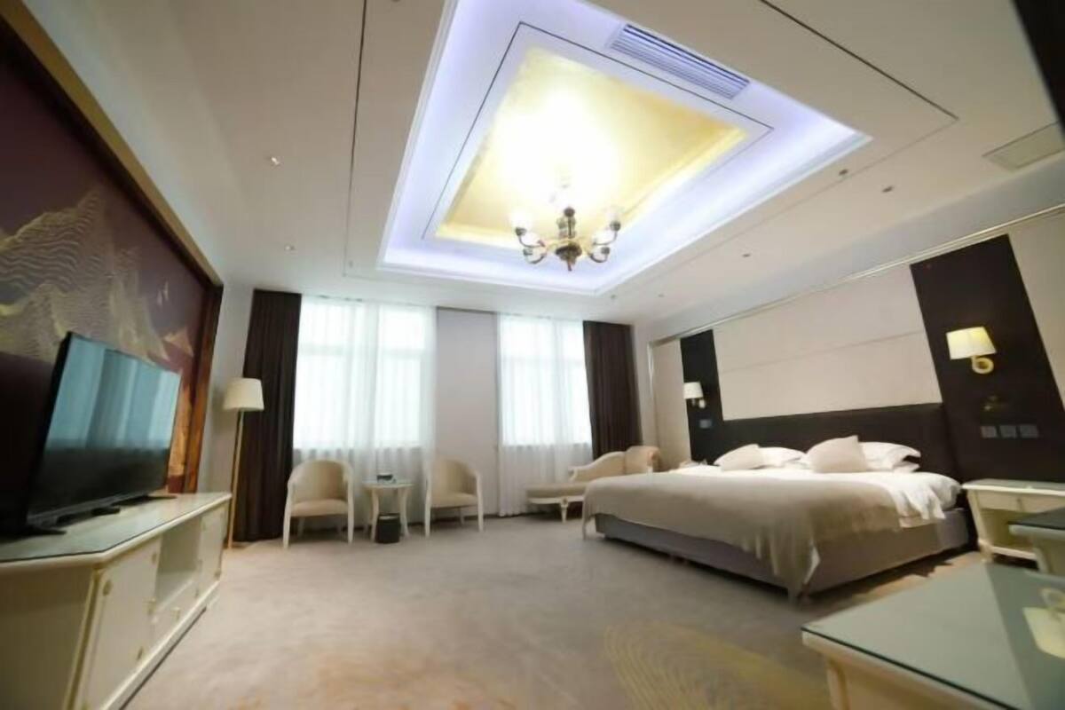 A hotel room with a large bed, a TV, a desk, and a ceiling light.