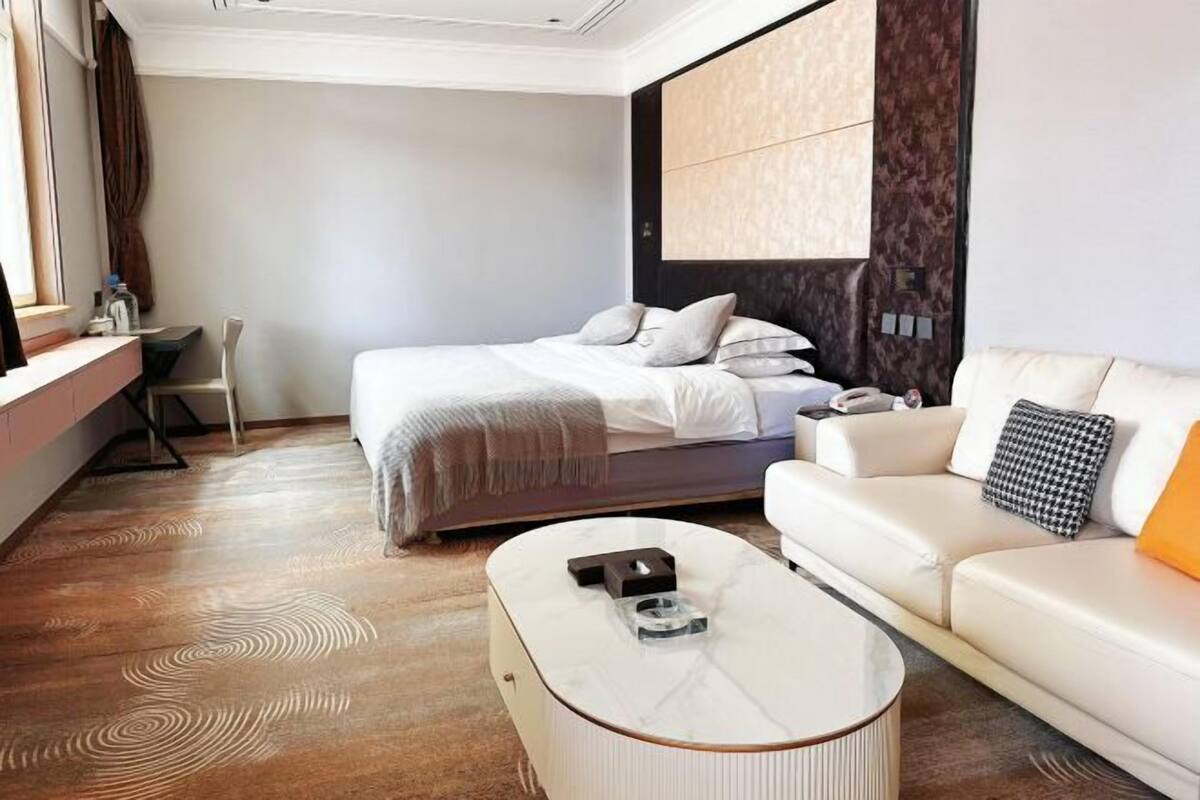 A hotel room with a bed, a white sofa, a marble coffee table, and a desk.
