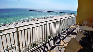A balcony with a view of a beach and pier, furnished with chairs and tables.