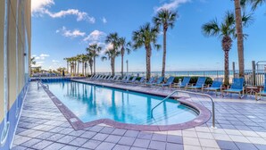 A swimming pool with blue tiles, surrounded by palm trees and blue lounge chairs.
