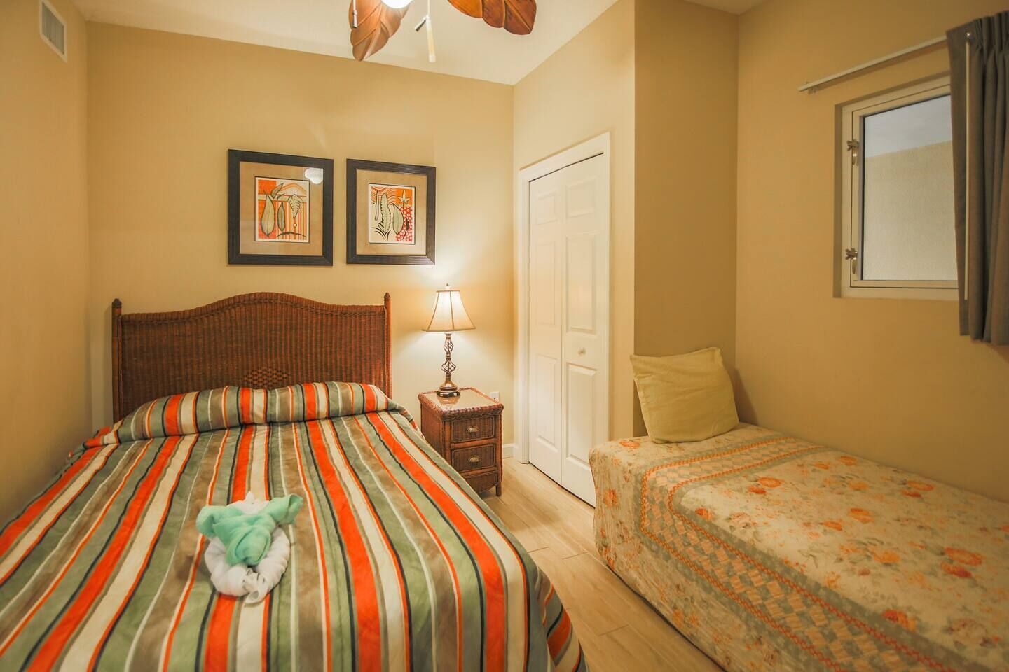 Un dormitorio con una cama grande, una cama más pequeña, una mesita de noche con una lámpara y dos cuadros enmarcados en la pared.