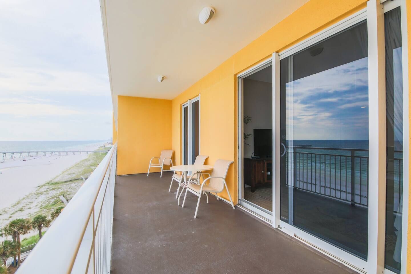 A balcony with a view of the beach and ocean, a table with chairs, and a television.