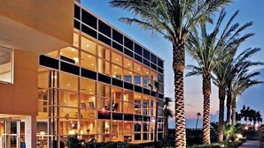 A modern hotel with a glass facade, multiple floors, and a palm tree-lined entrance.