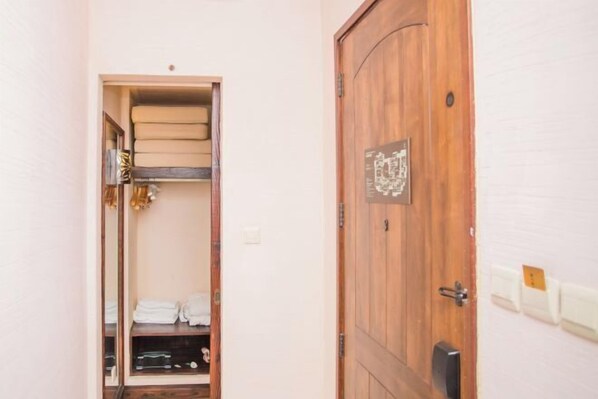A wooden door with a plaque, a closet with folded towels, and a shelf with a mirror.