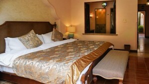 Een hotelkamer met een groot bed, een houten hoofdbord, een bankje, een nachtkastje, een lamp en een spiegel aan de muur.