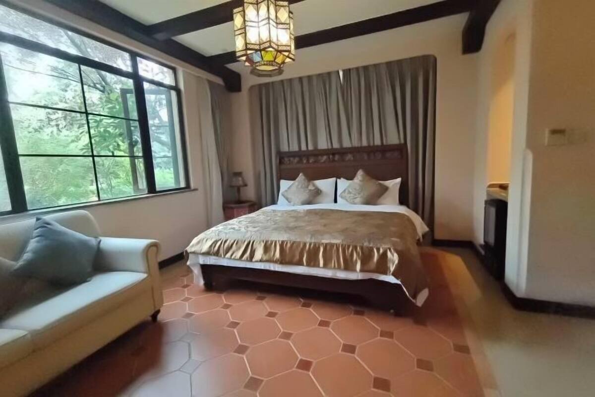 Een slaapkamer met een groot bed, een bank, een raam en een kroonluchter.