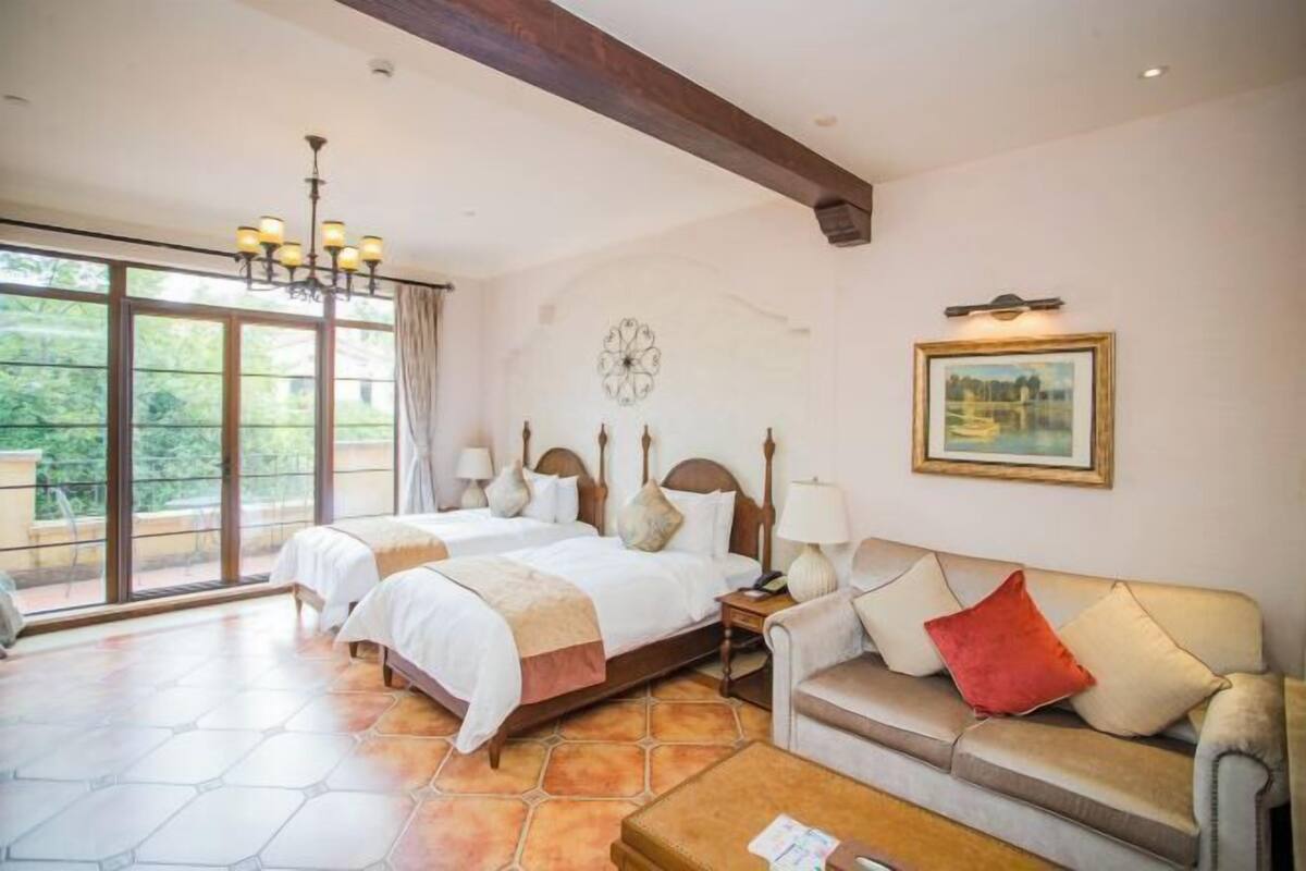 Een hotelkamer met twee bedden, een bank, een bijzettafeltje, een kroonluchter, een klok en een schilderij aan de muur.