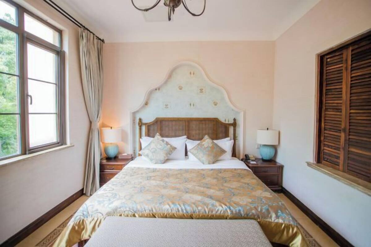 Een slaapkamer met een groot bed, twee nachtkastjes, een raam met gordijnen en een houten hoofdbord.