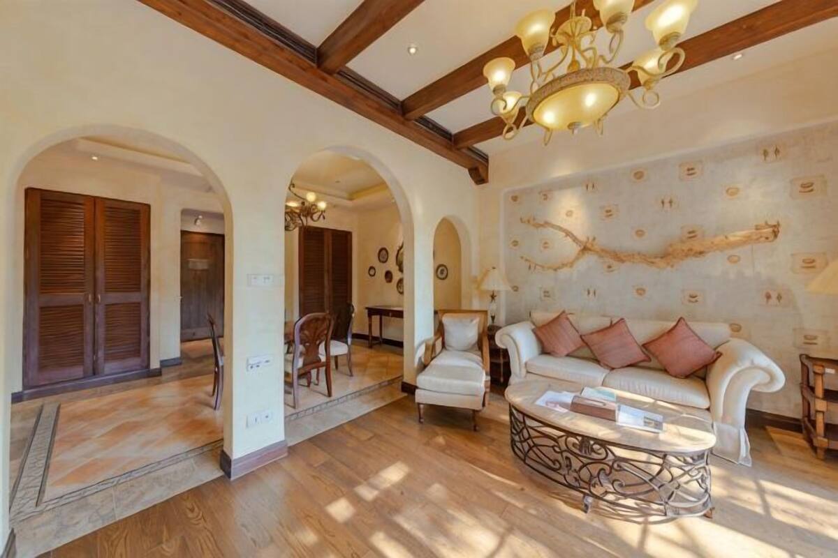 Een interieur met een houten vloer, een witte bank met kussens, een behang met patroon en een kroonluchter.