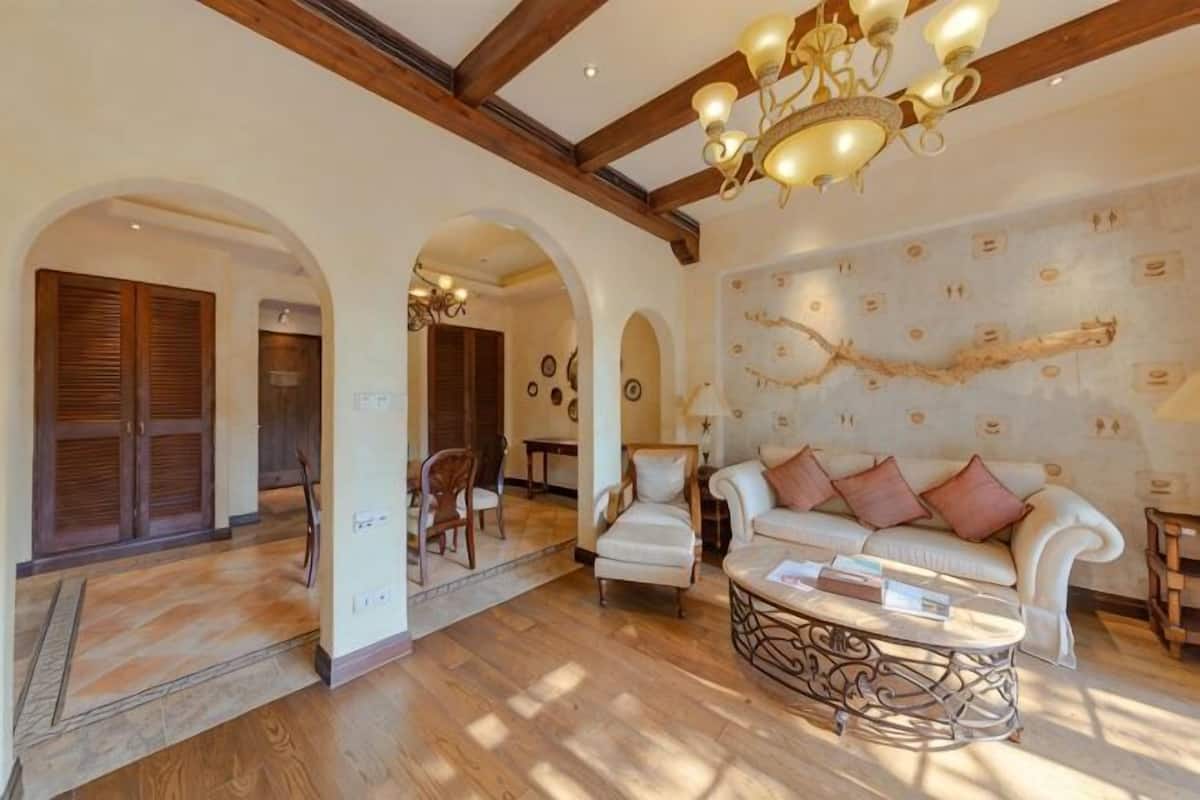 An interior with a wooden floor, a white sofa with cushions, a patterned wall, and a chandelier.