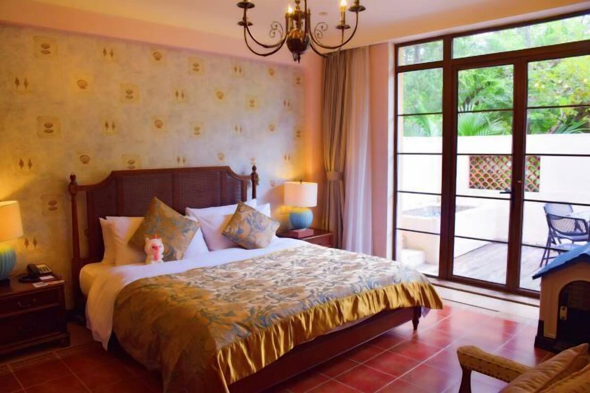 Hotelkamer met een groot bed, een kroonluchter, uitzicht door een schuifdeur en een tafeltje met een lamp.