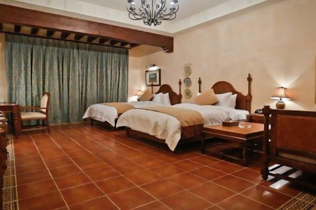 Een hotelkamer met twee bedden, een houten hoofdbord, een kroonluchter, een houten tafel en een stoel.