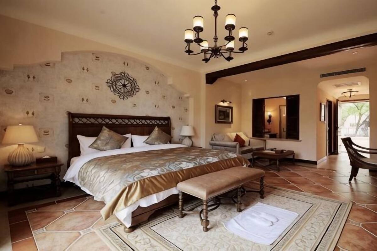Een slaapkamer met een groot bed, een bankje, een kroonluchter en een wand met een steenmotief.