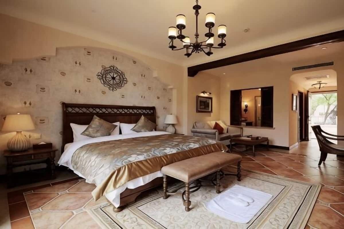 A bedroom with a large bed, a bench, a chandelier, and a stone-patterned wall.
