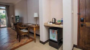 Een kleine hotelkamer met een eettafel, stoelen, een koelkast, een lamp en een deur.