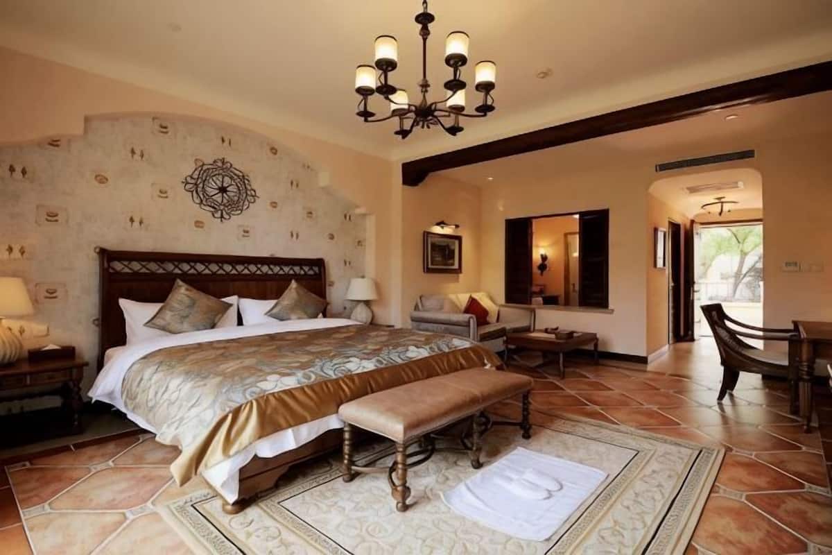 Een ruime slaapkamer met een groot bed, een bankje, een kroonluchter en uitzicht op buiten.