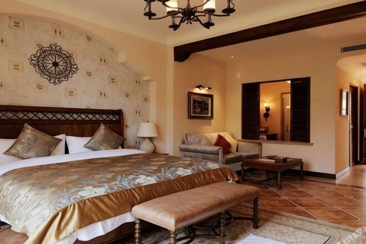 Een slaapkamer met een groot bed, een bankje, een stoel, een tafel en een spiegel.