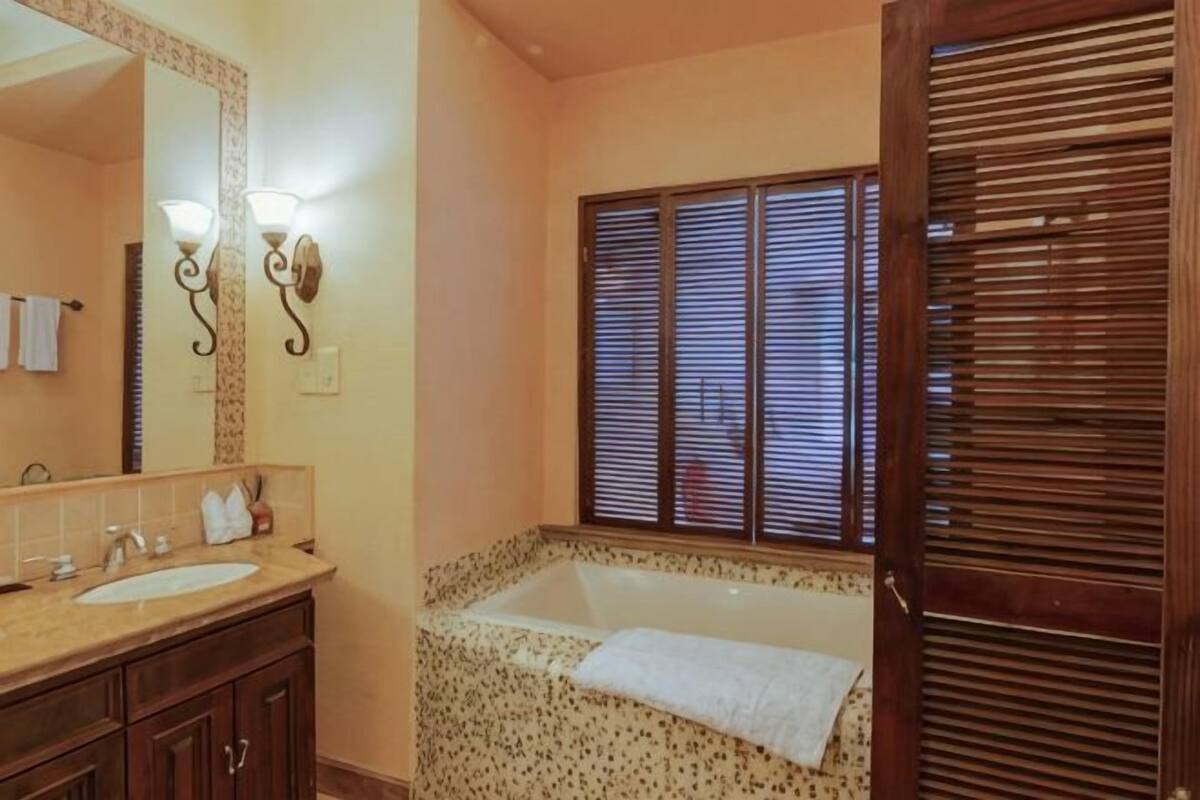 Een badkamer met een bad, een wastafel, een spiegel en een raam met zonwering.