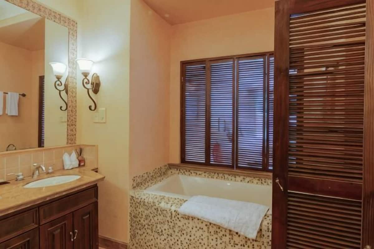 A bathroom with a bathtub, a sink, a mirror, and a window with blinds.