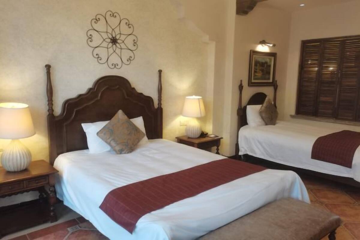 Een hotelkamer met twee bedden, een decoratief wandobject, een lamp en een raam met luiken.