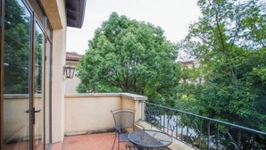 Een balkon met een tafel, stoelen, een glazen deur en uitzicht op bomen en gebouwen.