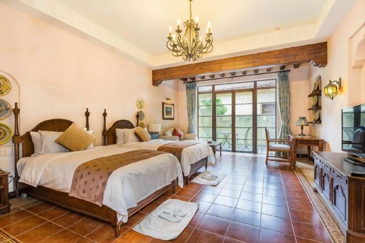 Een slaapkamer met twee bedden, een kroonluchter, een televisie en een groot raam.