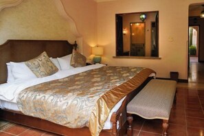A hotel room with a large bed, a wooden headboard, a bedside table with a lamp, and a window with a view of the outside.