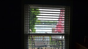 A window with horizontal blinds, a view of a deck with outdoor furniture, and a red umbrella.