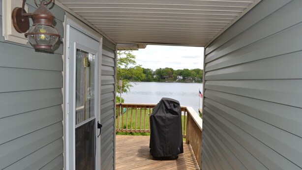 A covered deck with a view of a lake, a barbecue grill, and a lantern.