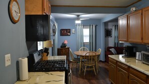 A compact kitchen with wooden cabinets, a stove, and a dining area with chairs.