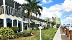 A hotel with a balcony, a palm tree, and a pathway leading to a dock with boats. - STUNNING WATERFRONT 2 BEDROOM BEAUTY.  CLOSE TO EVERYTHING. (Fort Lauderdale)