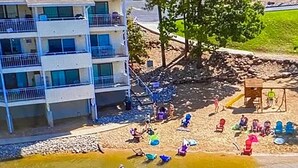 Ein Strandabschnitt mit Spielplatz, einem Gebäude mit Balkonen und einer kleinen Wasserfläche.