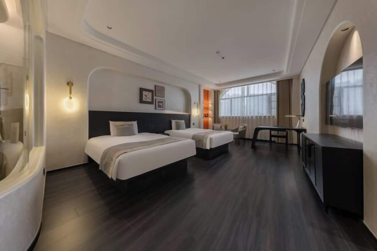 A hotel room with two beds, a desk, a chair, and a large window.