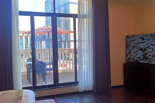 Une chambre d’hôtel dotée d’une grande porte-fenêtre coulissante donnant sur un espace extérieur avec une table et des chaises, un balcon avec une balustrade et un téléviseur posé sur un meuble.