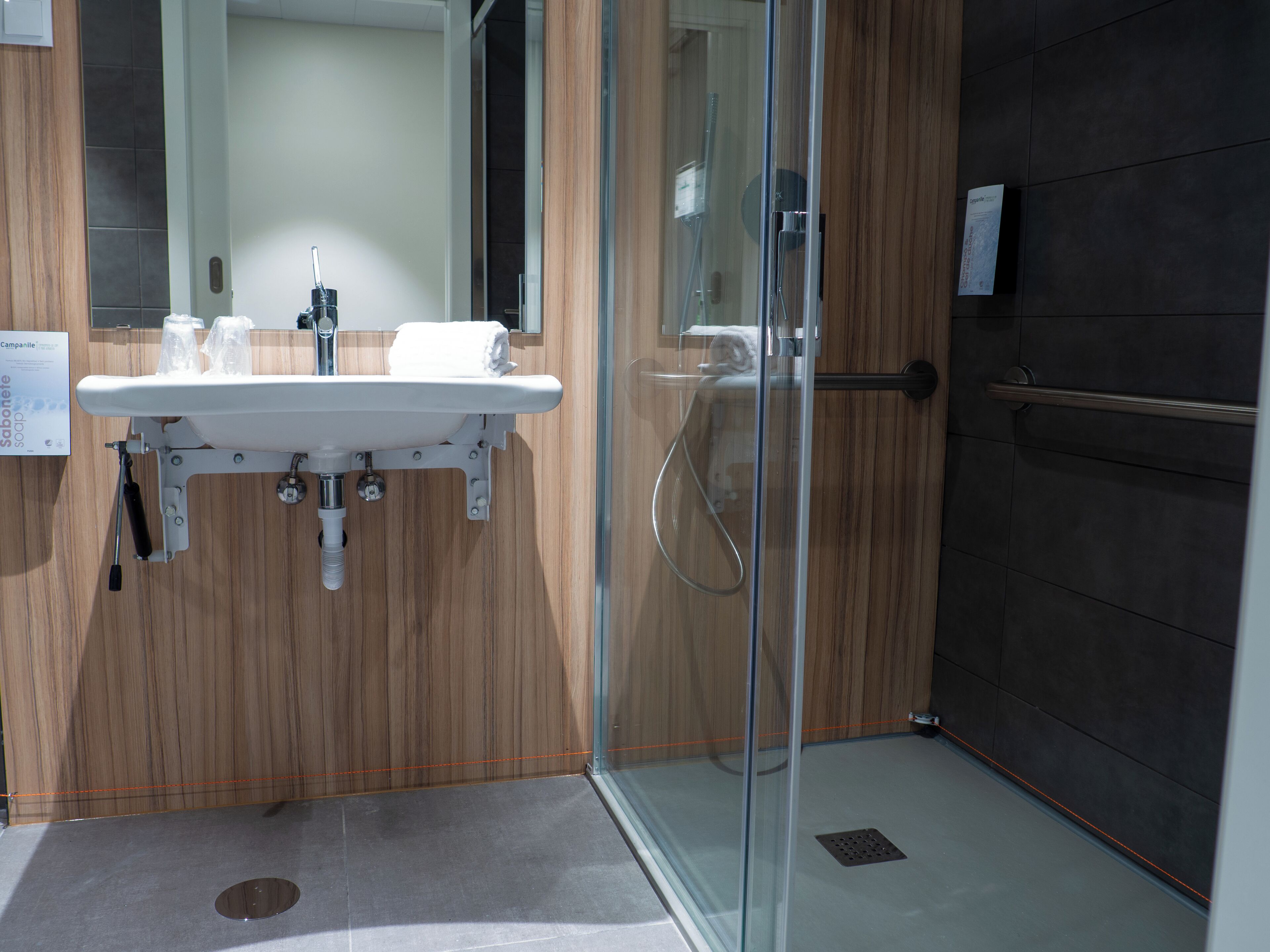 Une salle de bain moderne avec une douche à l’italienne en verre, un lavabo blanc et un meuble-lavabo en bois.