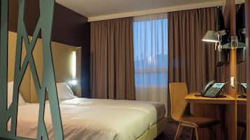 Habitación de hotel con cama, escritorio con teléfono, silla y un amplio ventanal con cortinas.