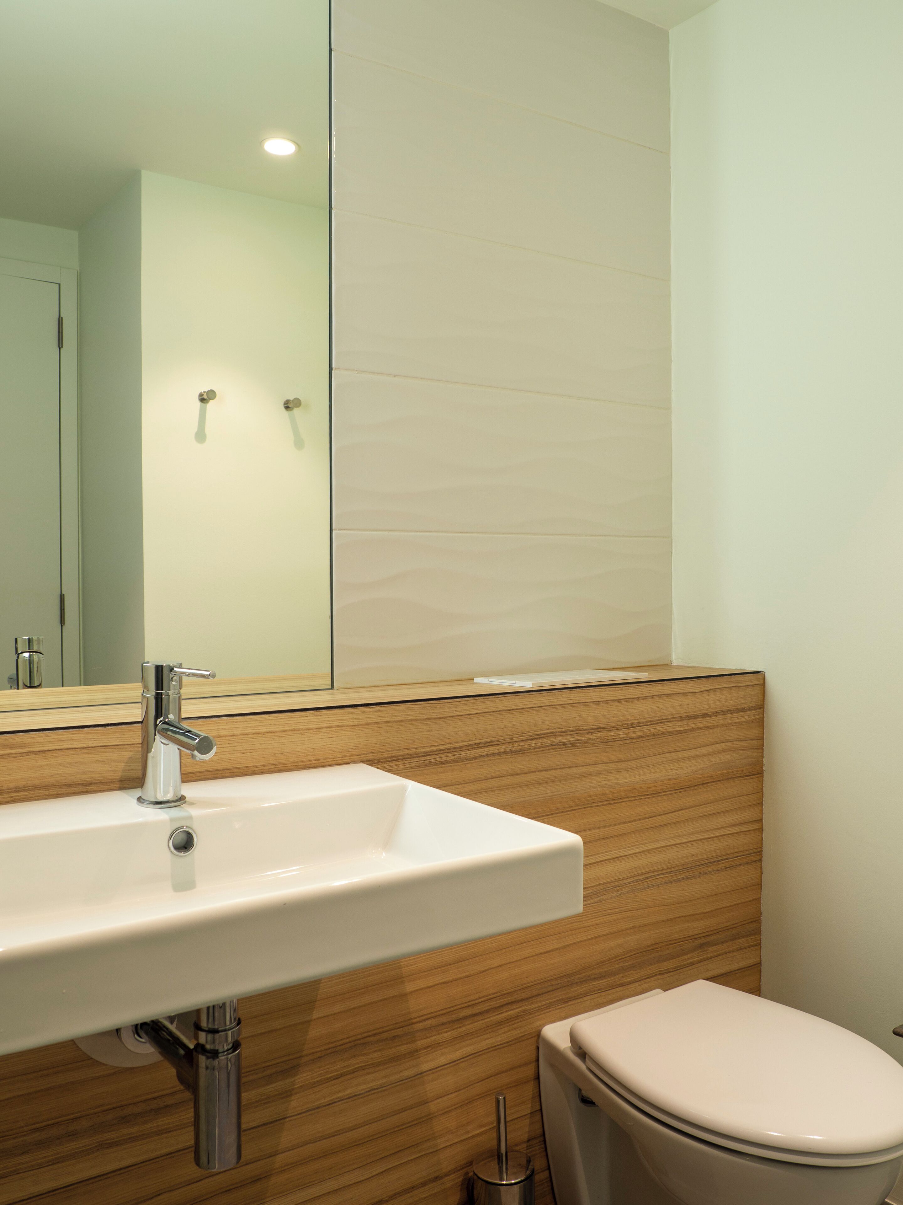 A bathroom with a white sink, wooden paneling, a mirror, and a toilet.