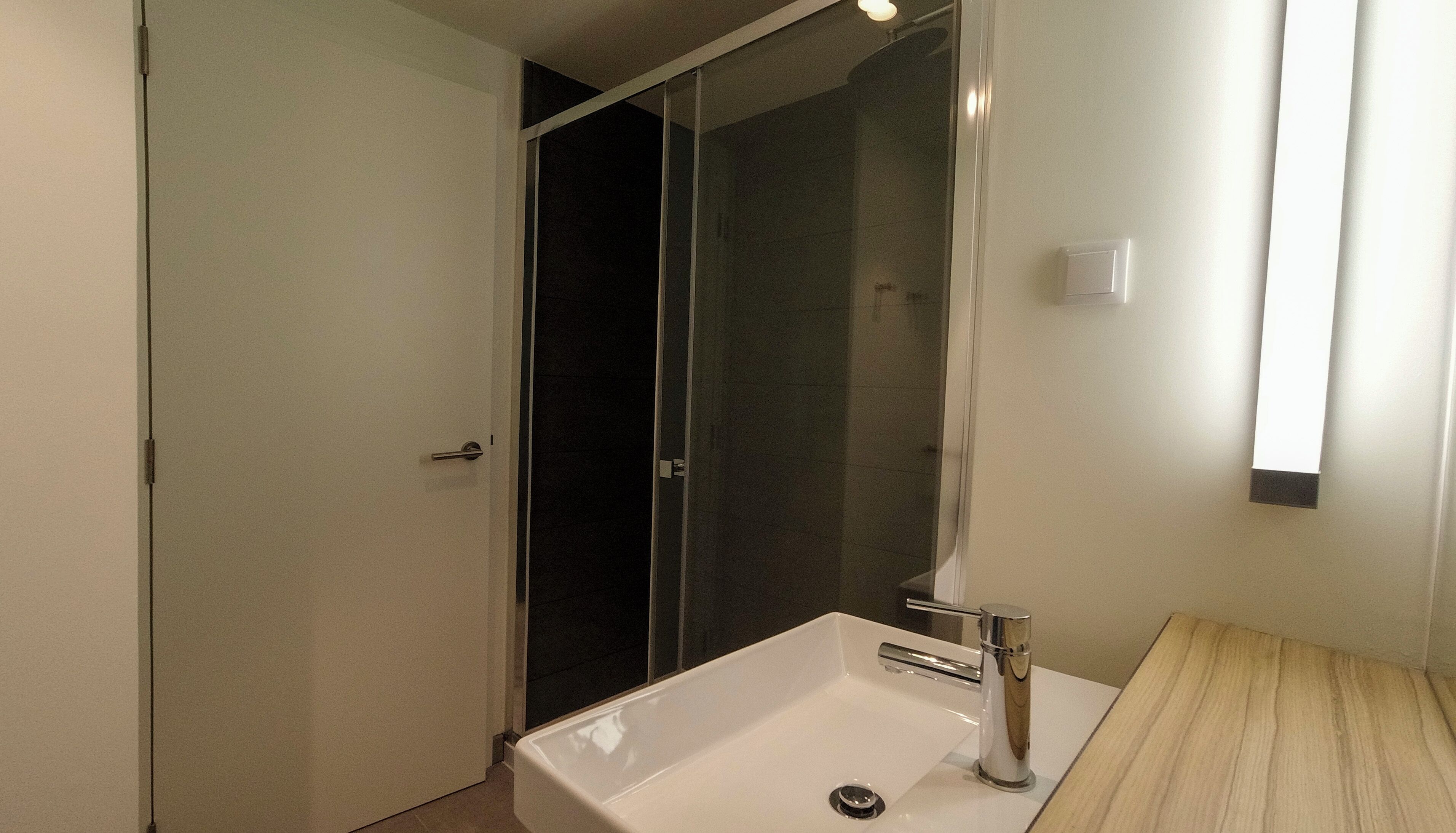 A modern bathroom with a white sink, a glass shower enclosure, and a wooden vanity.