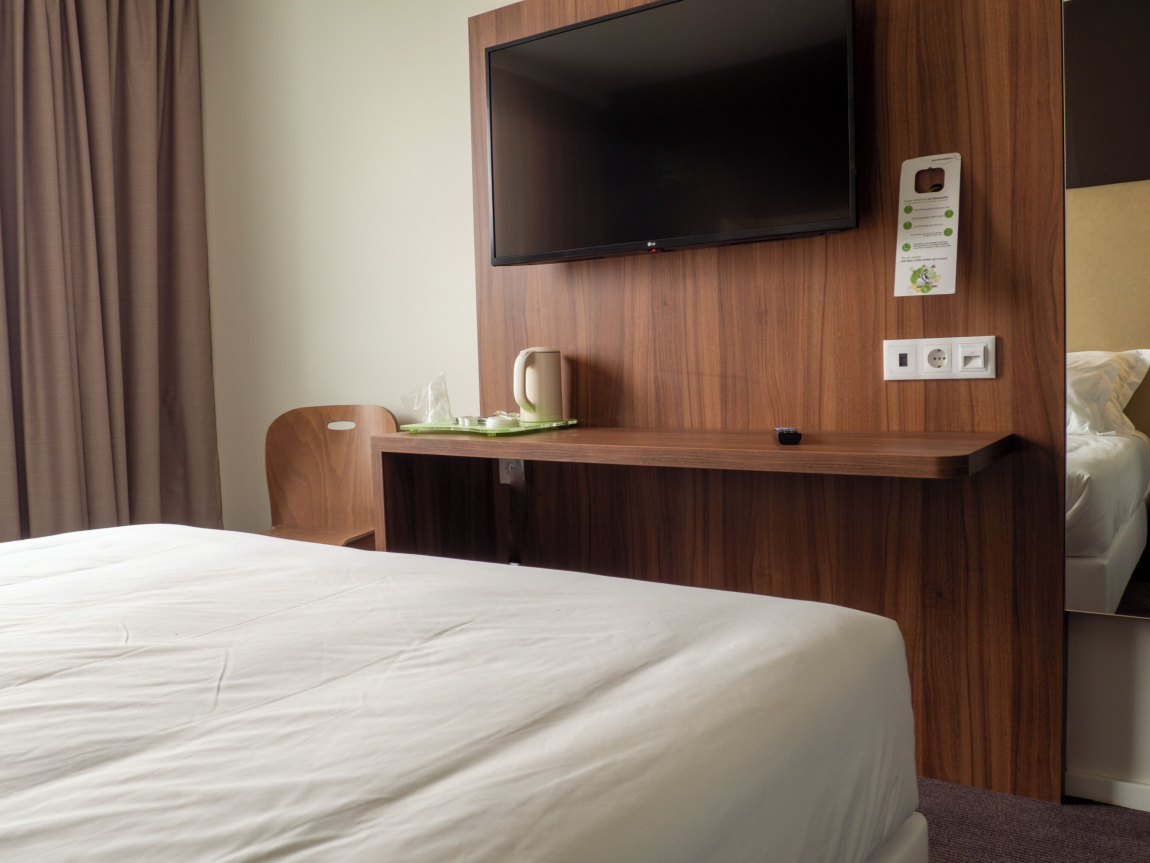 A hotel room with a bed, a wooden desk with a flat-screen TV, a coffee maker, and a power outlet.