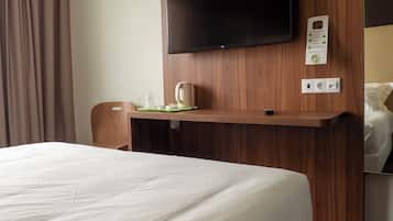Habitación de hotel con cama, escritorio de madera, televisor de pantalla plana, cafetera y toma de corriente.